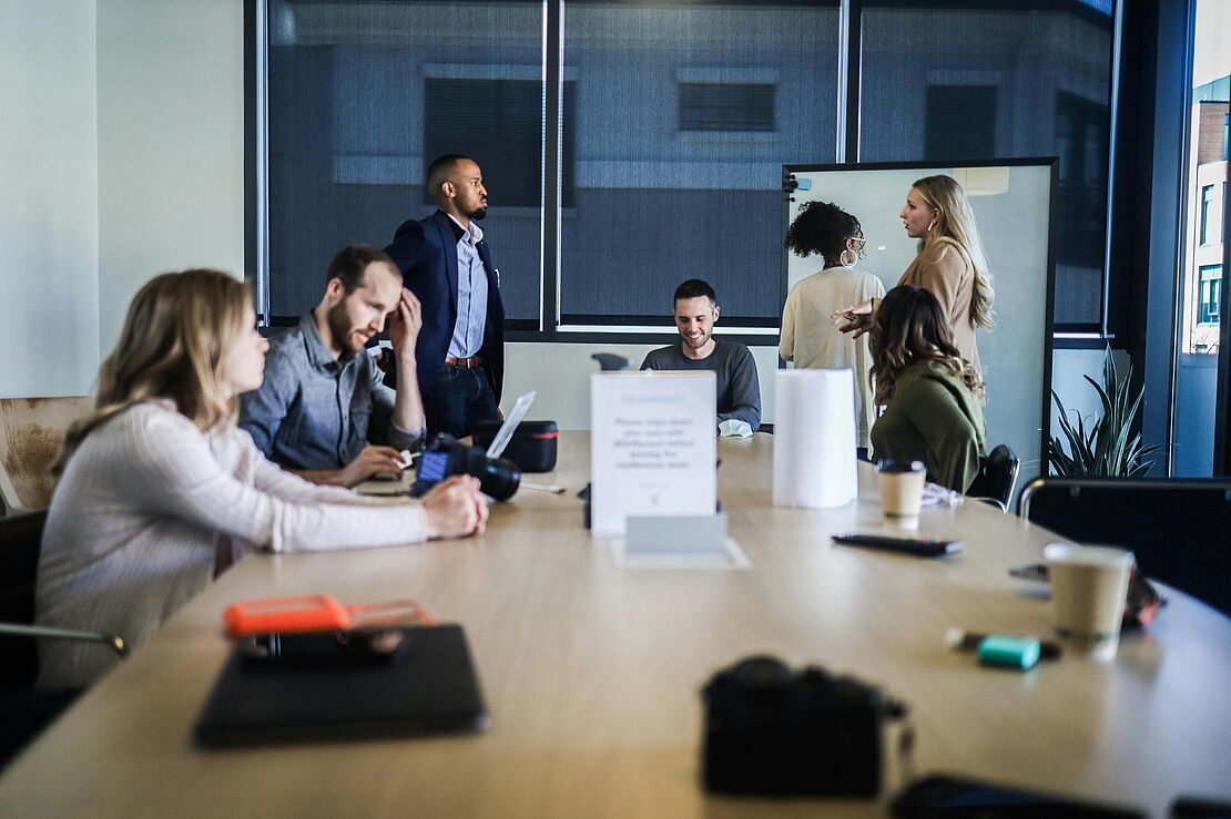 Mehrere Personen arbeiten gemeinsam an einem Tisch mit Laptop und Unterlagen in einem modernen Büroraum als Beispiel für Inhouse‑Schulungen im Unternehmen