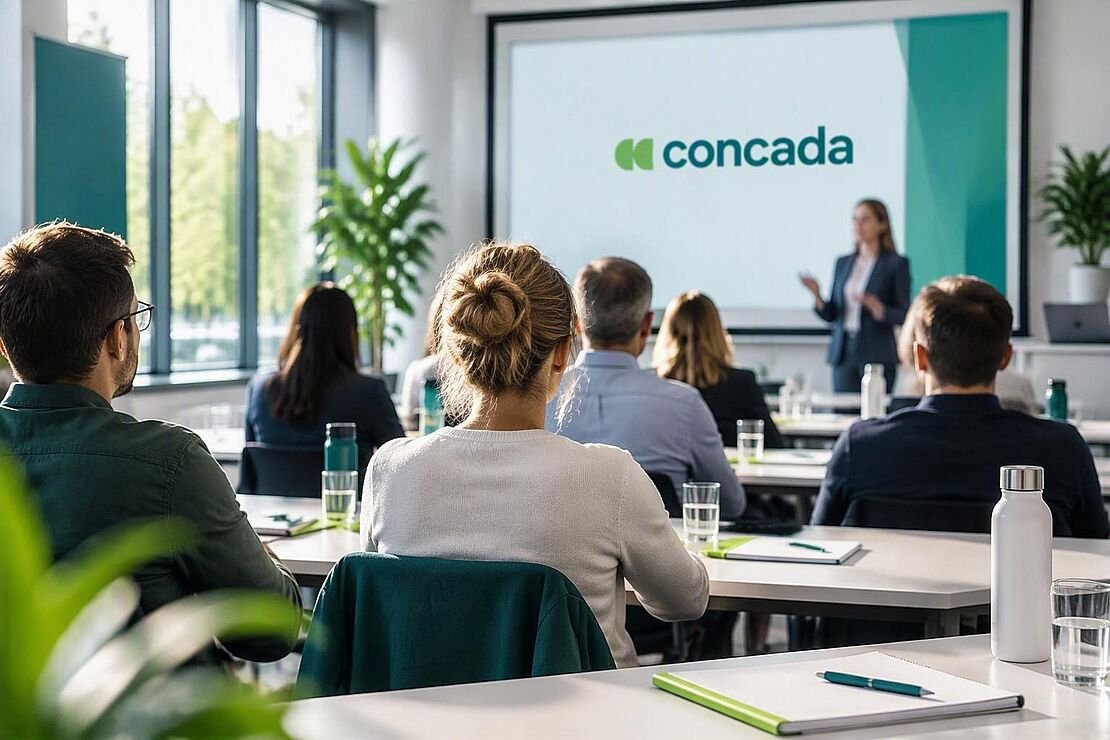 Teilnehmende von hinten bei einem concada Seminar in einem hellen Seminarraum. Eine Präsentation mit concada Logo findet statt, während Schreibunterlagen und Getränke auf den Tischen bereitliegen.