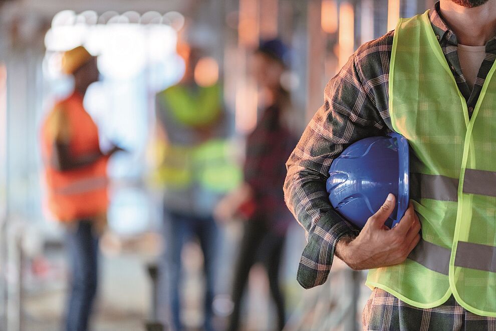 Person mit Schutzweste und Schutzhelm auf einer Baustelle als Symbol für die Tätigkeit einer Fachkraft für Arbeitssicherheit (Sifa).