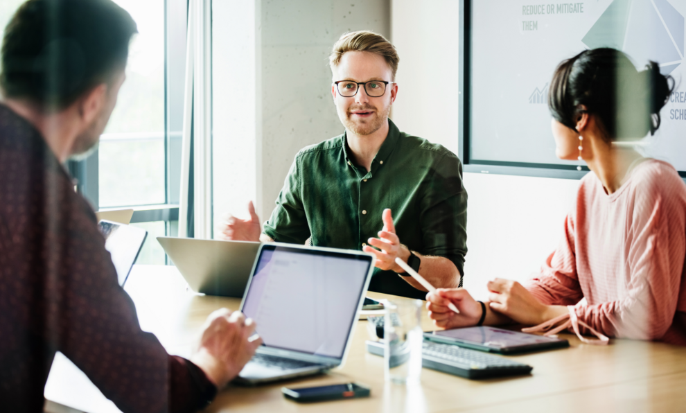 Drei Personen sitzen sich an einem Besprechungstisch gegenüber