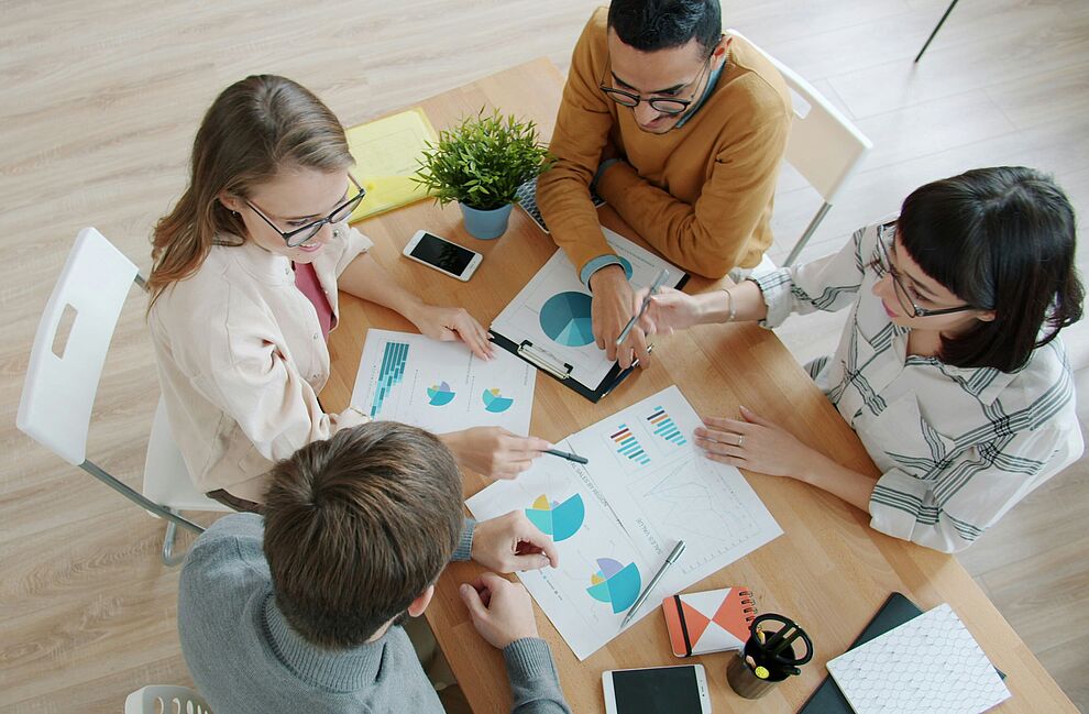 Eine Gruppe von vier Personen sitzen um einen Tisch und werten Statistiken und Diagramme aus