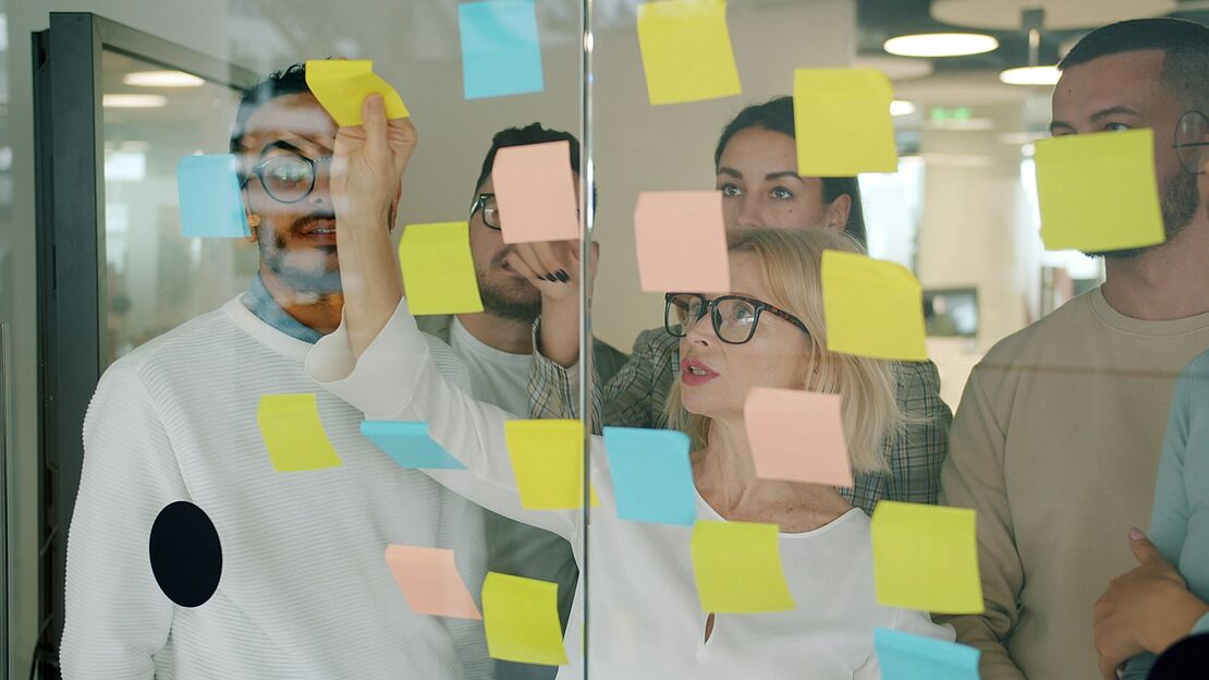 Team analysiert Arbeitsabläufe an einer Glaswand mit Haftnotizen im Rahmen eines Behavior Based Safety Workshops
