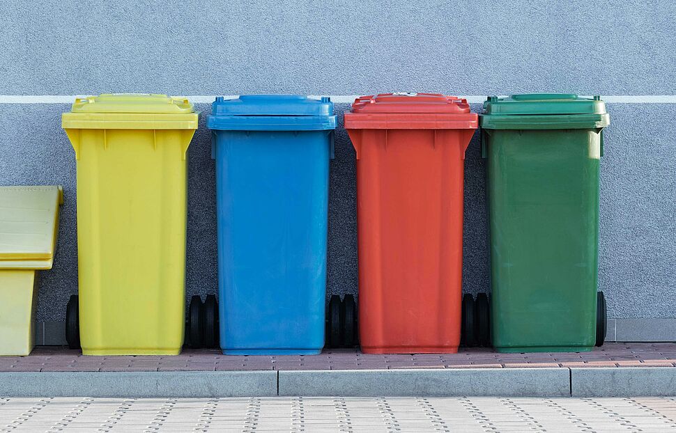 Das Bild zeit vier Mülltonnen in den Farben gelb,blau,rot und grün nebeneinander stehend.
