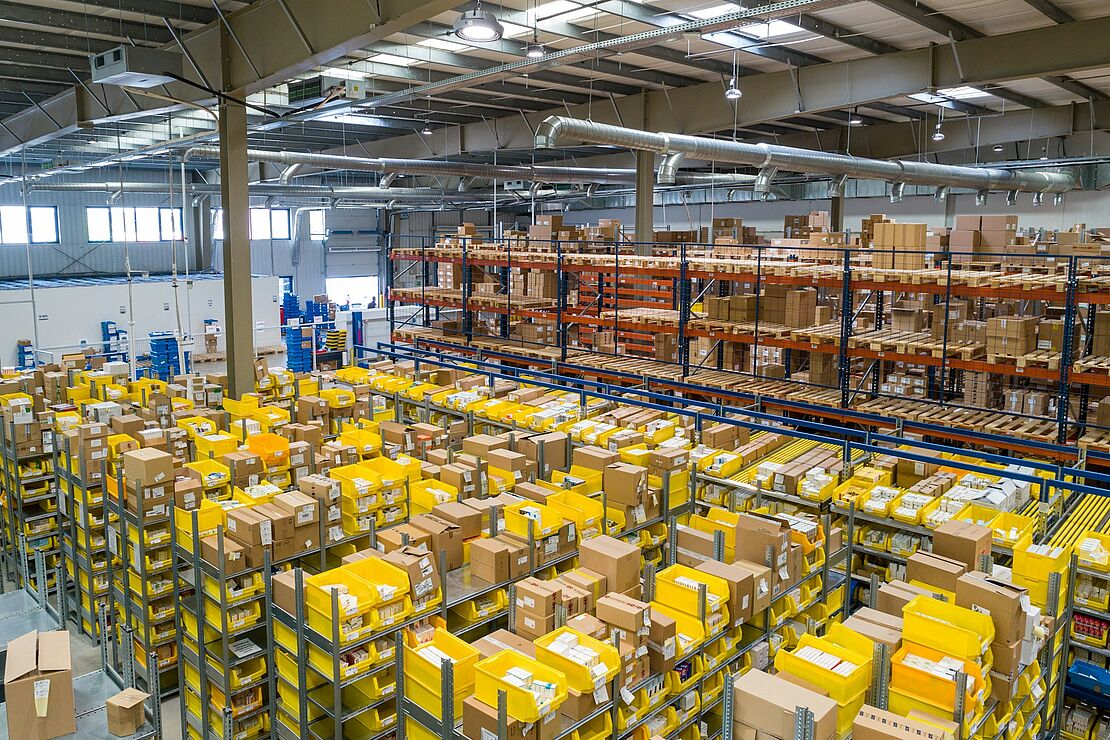 Ein großes Lager mit mehrstöckigen Regalanlagen, gefüllt mit Kartons und gelben Behältern, zeigt die Struktur und Organisation einer modernen Logistikhalle.