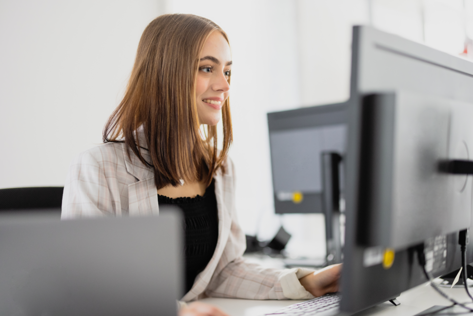 Junge Frau sitzt am Schreibtisch und schaut auf einen Monitor