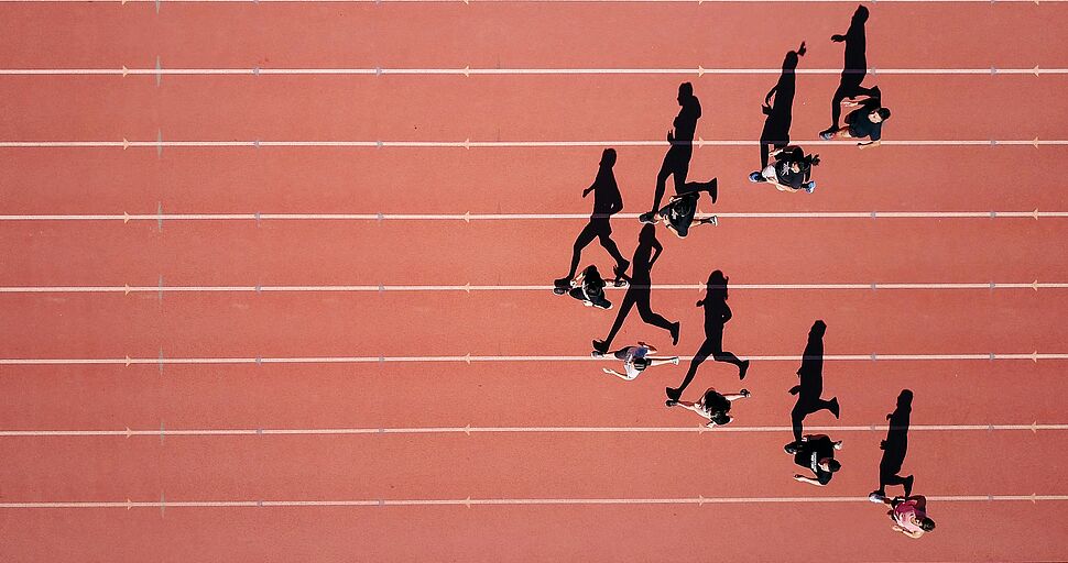 Mehrere Personen laufen auf Bahnen eines Sportplatzes