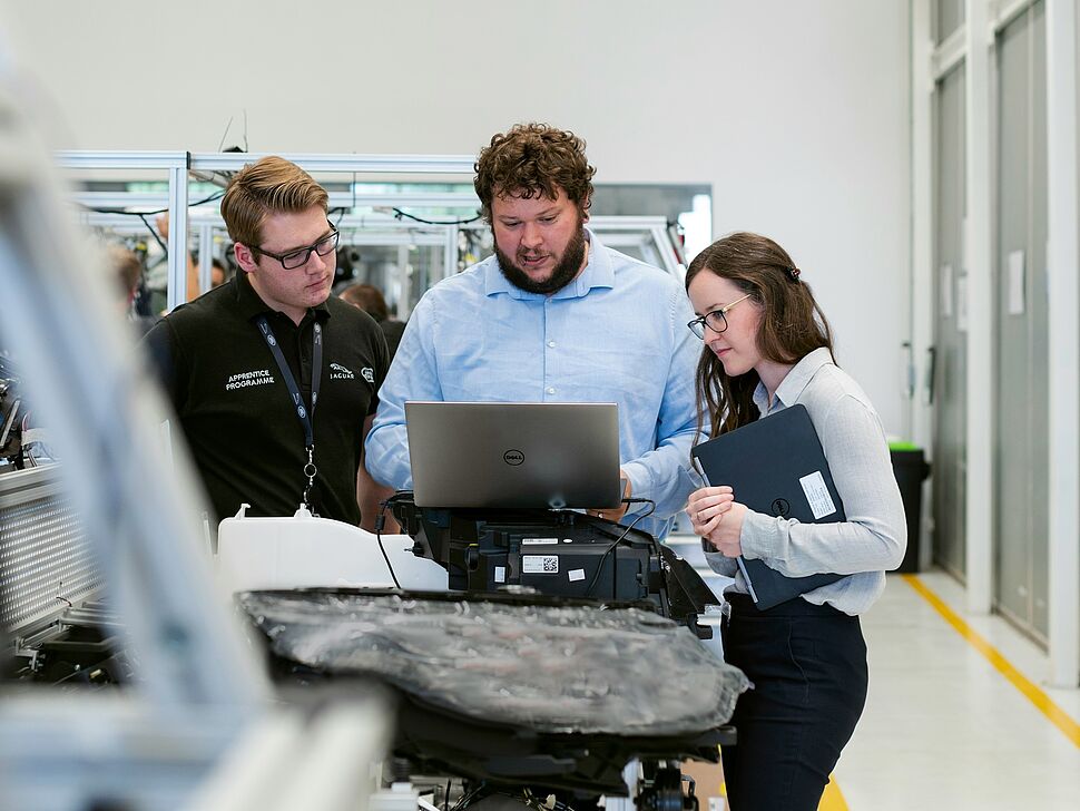 Eine Gruppe von drei Personen stehen um einen Computer herum