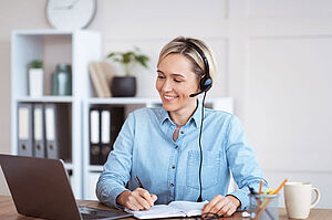 Online-Akademie Eine Frau mit Headset am Schreibtisch