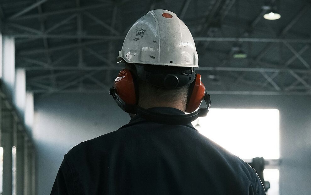 Sicherheitsbeauftragter in der Industrie mit Schutzhelm und Gehörschutz überprüft die Einhaltung von Arbeitsschutzmaßnahmen in einer Produktionshalle 