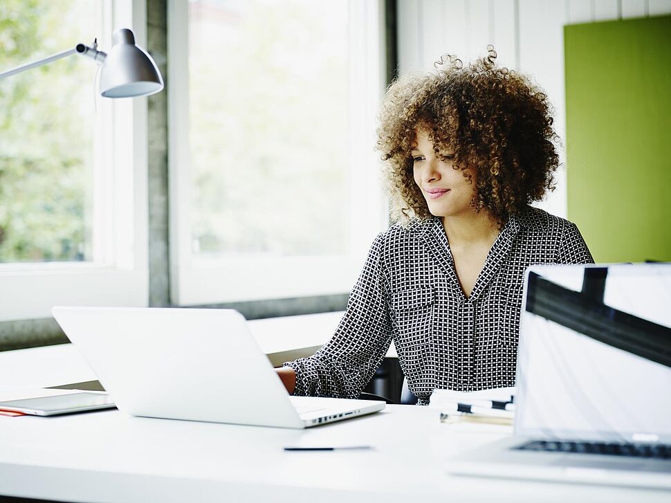 Frau sitzt am Schreibtisch und arbeitet am Laptop