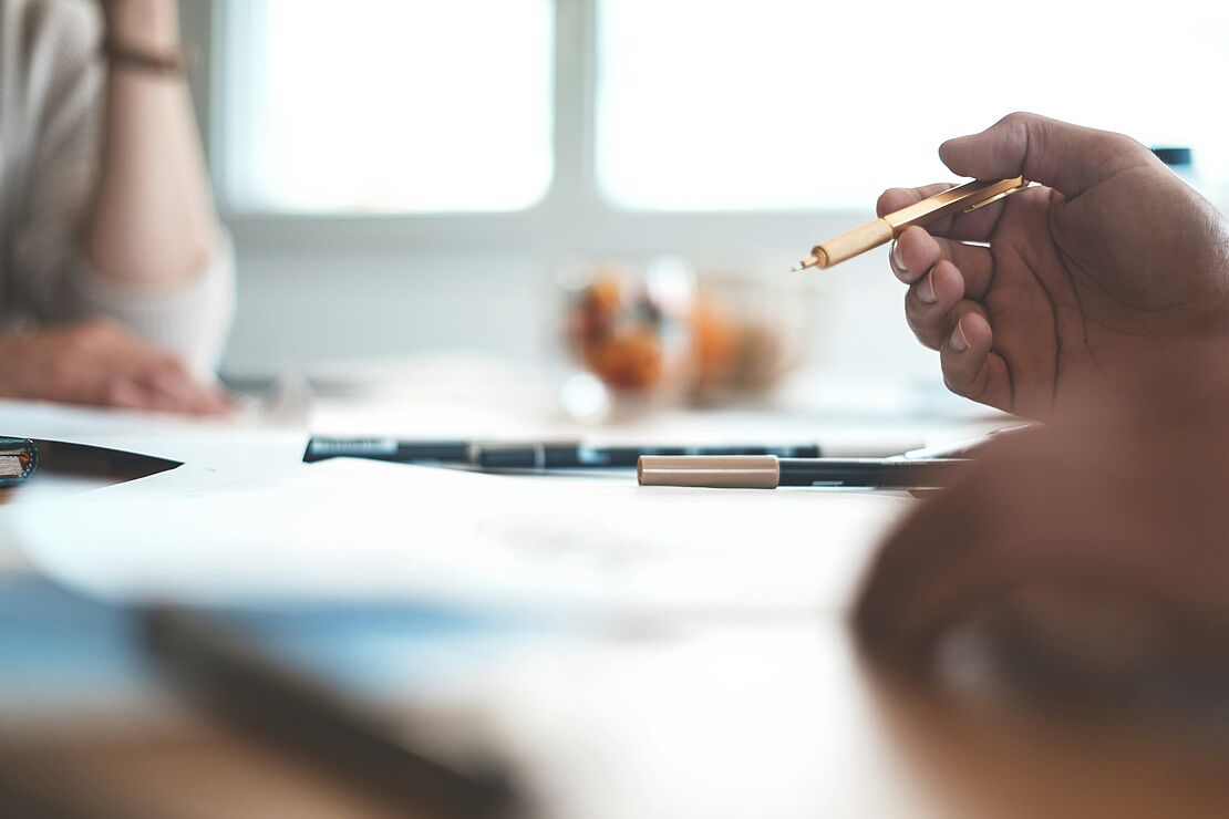 Personen sitzen an einem Tisch mit Unterlagen und Laptop und bearbeiten Dokumente als Beispiel für Planung und Umsetzung geförderter Weiterbildung im Unternehmen