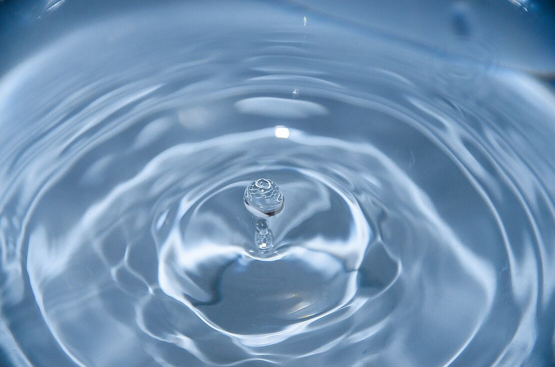 Ein einzelner Wassertropfen trifft auf eine Wasseroberfläche und erzeugt konzentrische Wellen