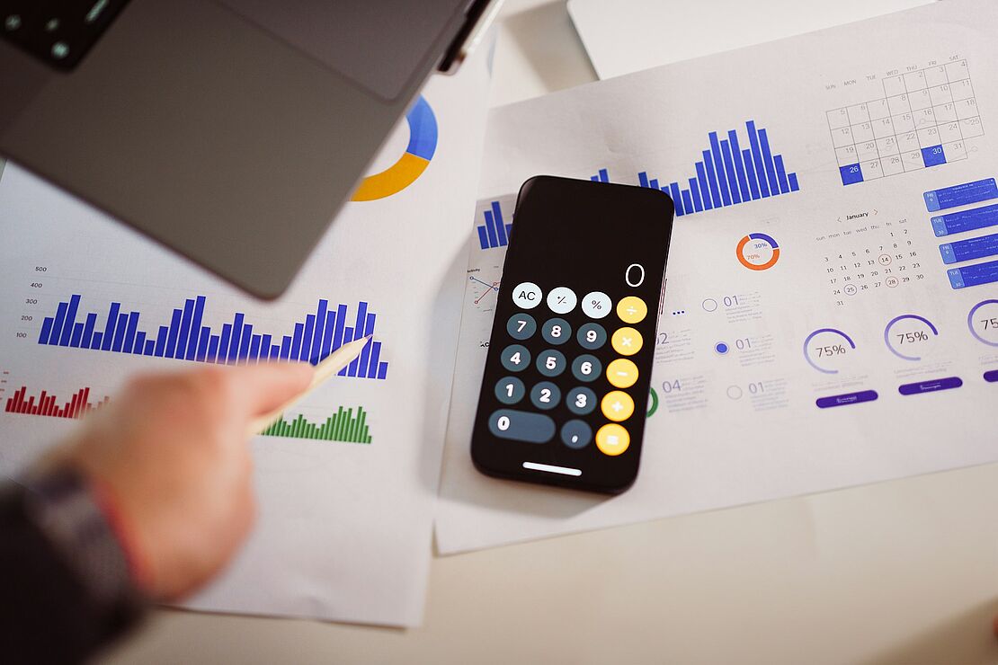 Papierauswertungen mit Diagrammen und Kennzahlen liegen neben einem Smartphone mit Rechner-App als Symbol für die Bewertung interner Audits